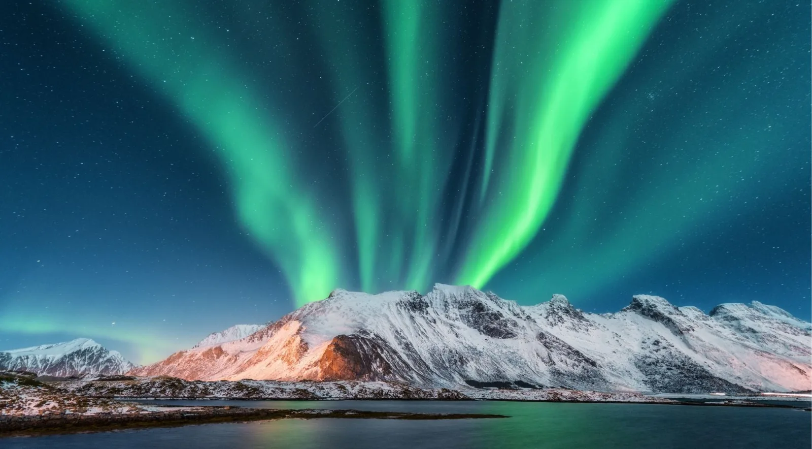 Aurora borealis glowing green over a Lofoten fishing village and snow-dusted peaks at night