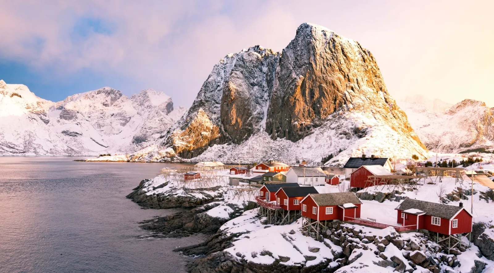 Red rorbuer fishing cabins beneath sharp, snow-capped Lofoten mountains in winter light