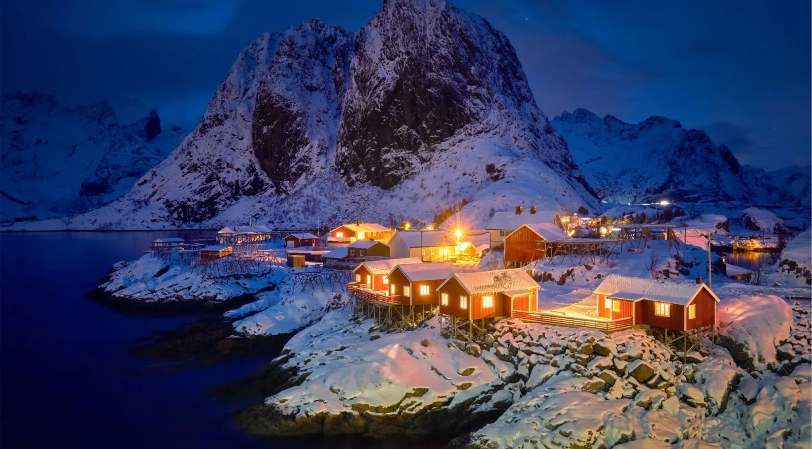 A Lofoten village glowing at blue hour beneath snow-covered mountains