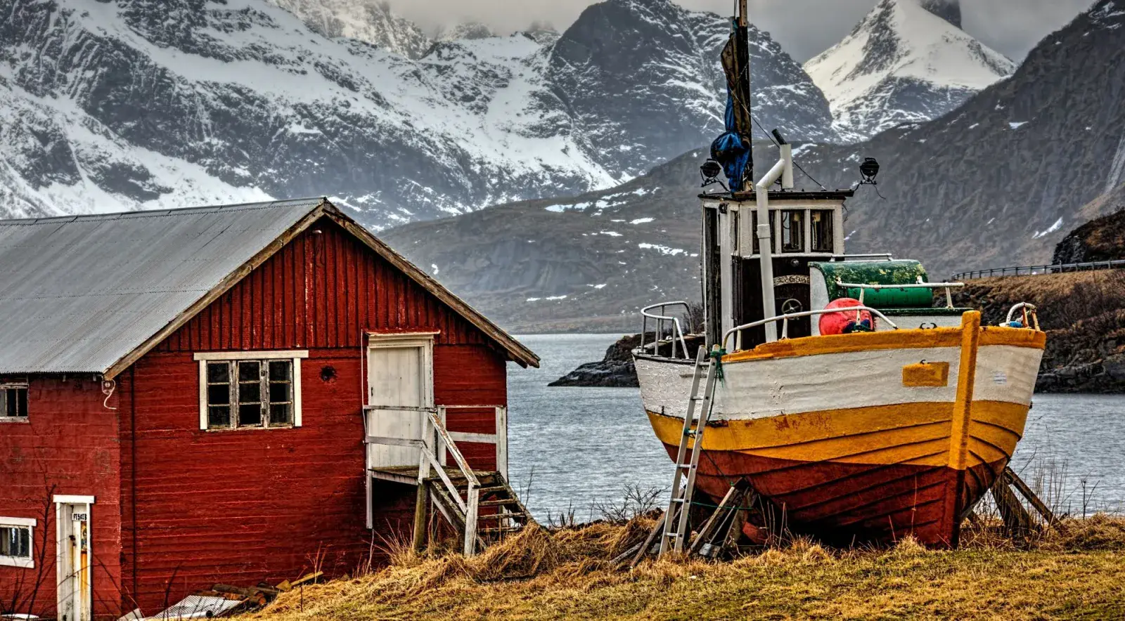 A red rorbu and wooden boat below a snow-covered mountain in Lofoten