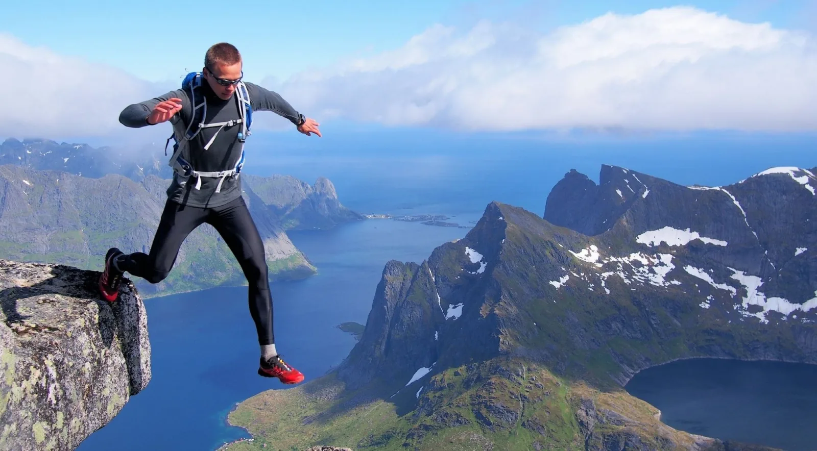 A hiker leaping between rocks high above Reinefjord on the Reinebringen trail