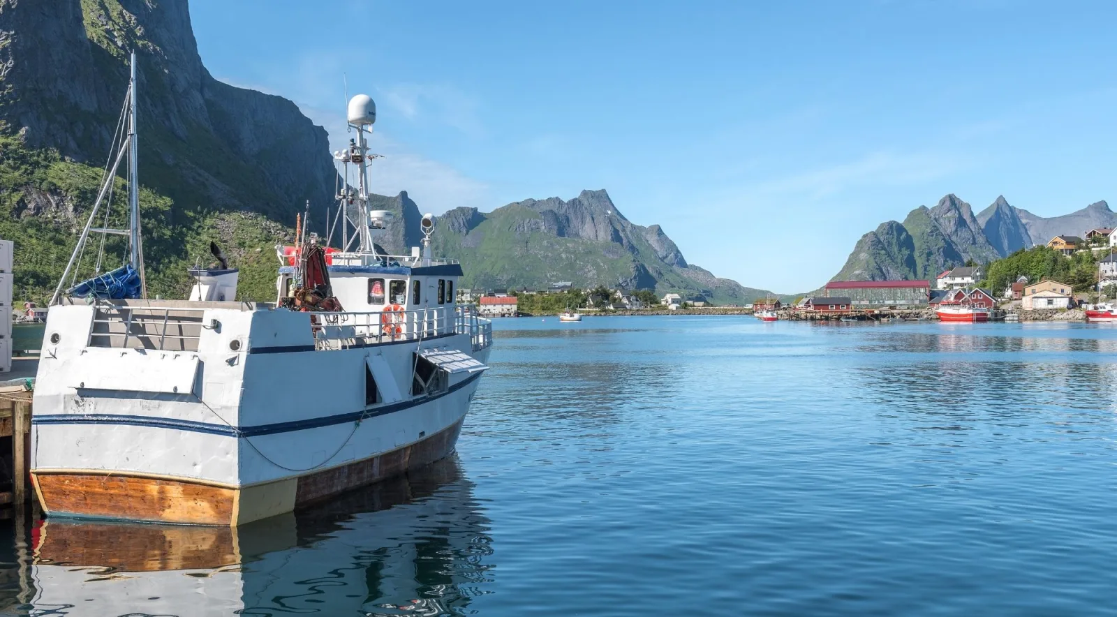 A white fishing boat in a sheltered Lofoten harbour ringed by mountains